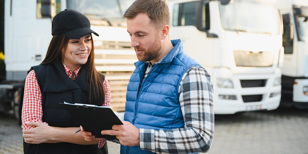Two people looking at a tablet with buses in the backdrop.