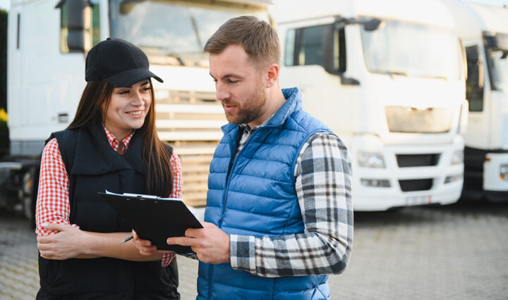 Two people looking at a tablet with buses in the backdrop.