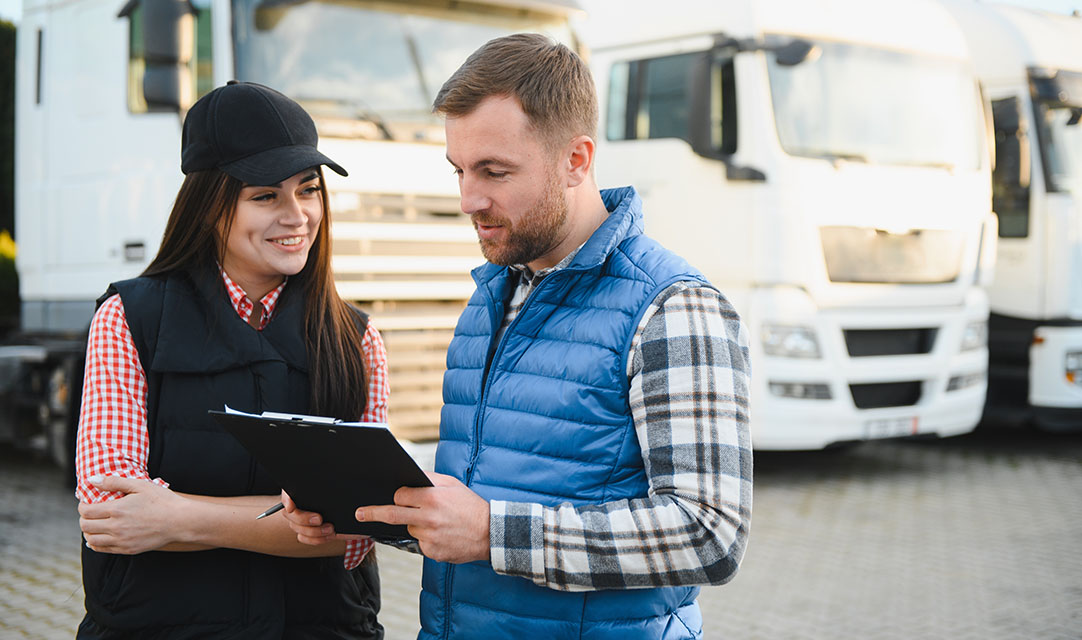 Two people looking at a tablet with buses in the backdrop.